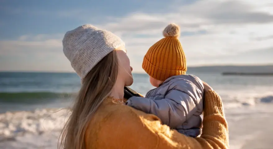Madre abraza a su bebé en la playa, disfrutando de un momento de paz. Un respiro merecido, como una excedencia y vacaciones no disfrutadas, antes de volver a la rutina.