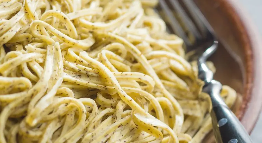 Un primo piatto invitante di tagliolini al limone, conditi con una salsa cremosa e profumata, pronti per essere gustati con una forchetta.