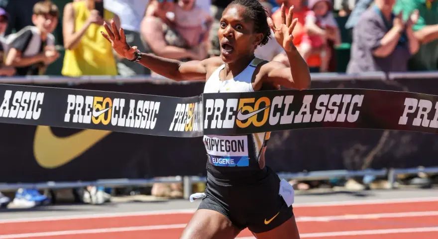Faith Kipyegon przekracza linię mety z uniesionymi rękami, triumfując na bieżni.
