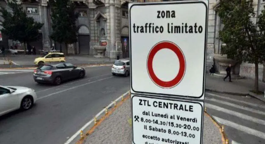 Cartello che indica "zona traffico limitato" con orari specifici. Auto in transito su strada urbana.