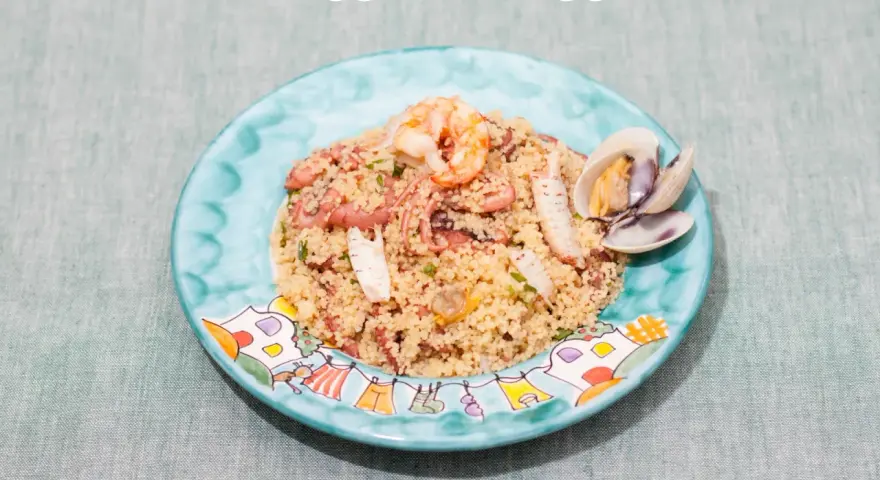 Un saporito cous cous di pesce con gamberi, polpo e cozze, servito su un piatto decorato.