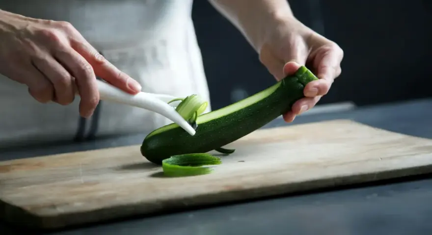 Manos pelando un calabacín para preparar deliciosas recetas con calabacín.