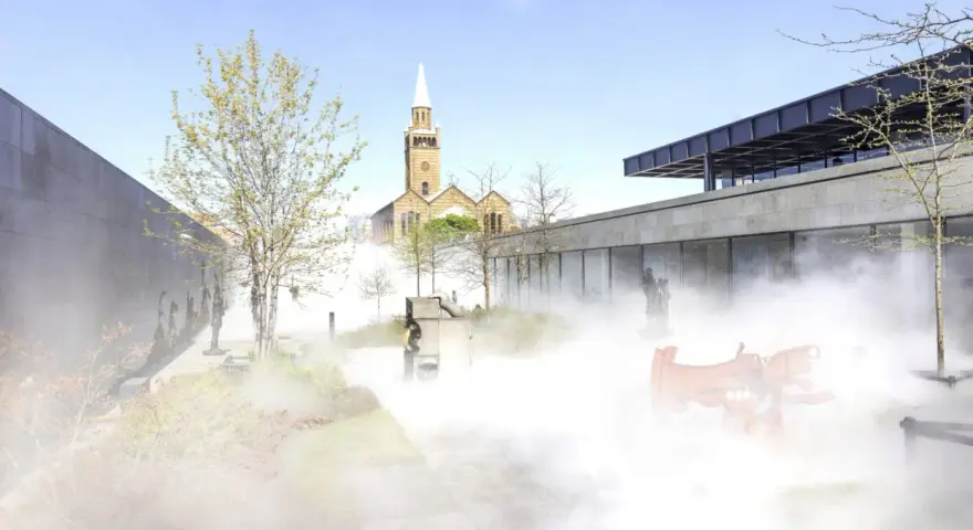 Ein nebliger Garten mit Skulpturen und einer Kirche im Hintergrund, ein friedlicher Ort für Christi Himmelfahrt in Berlin.
