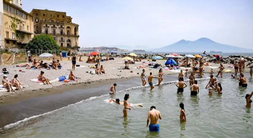 Gente che si gode il sole e il mare sulle spiagge libere di Napoli, con il Vesuvio sullo sfondo.