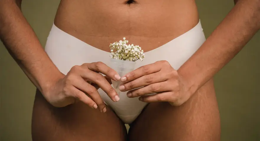 Kobieta trzyma kubeczek menstruacyjny z kwiatami, symbolizujący naturalność cyklu. To część odpowiedzi na pytanie: co to okres.