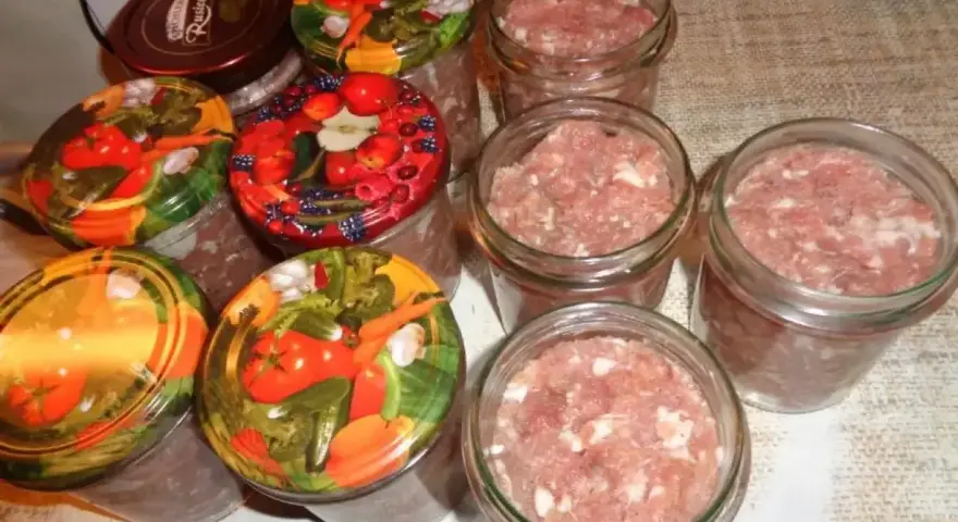 Słoiki z mielonym mięsem, gotowe do pasteryzacji. To pierwszy krok, jak zrobić kiełbasa w słoiku z galaretką. Kolorowe nakrętki z warzywami i owocami.
