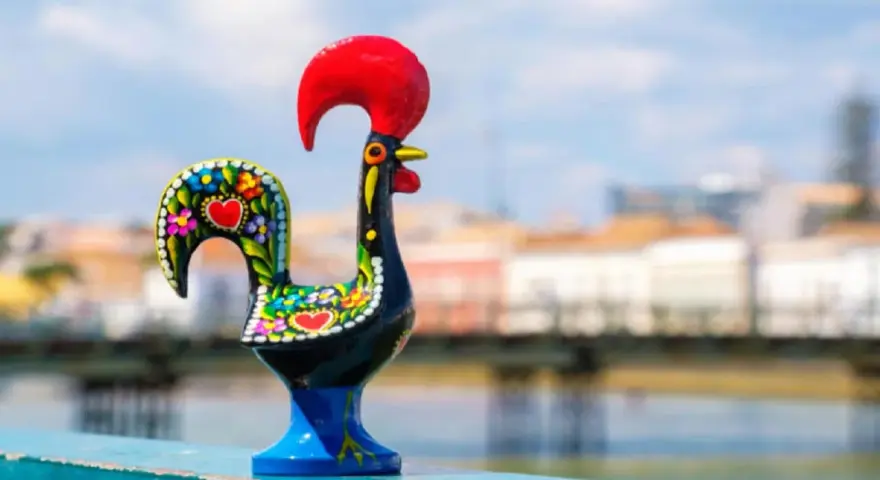 Un gallo de cerámica negro, decorado con flores y corazones, se alza orgulloso con su cresta roja.