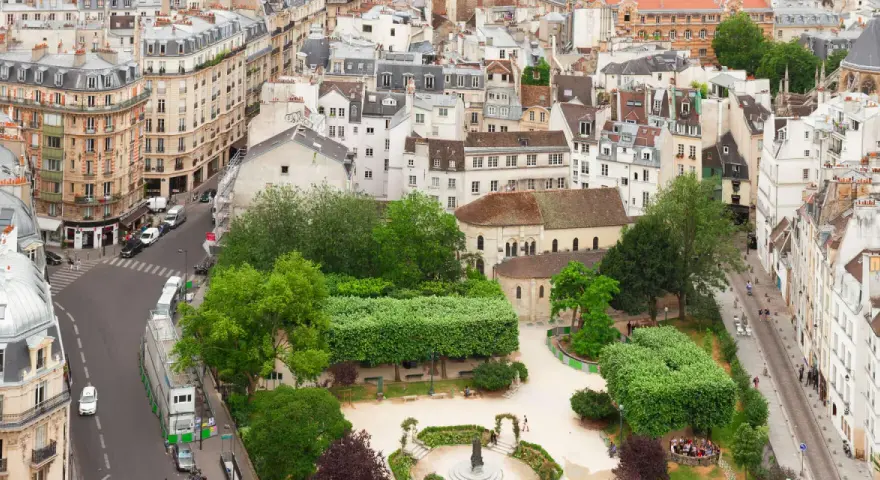 Vista aérea de un barrio latino con edificios antiguos, calles estrechas y un parque verde con gente disfrutando del día.