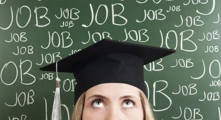 Absolventin mit Doktortitel blickt nach oben, während die Tafel voller "JOB" steht. Die Suche nach Arbeit nach dem Studium ist intensiv.