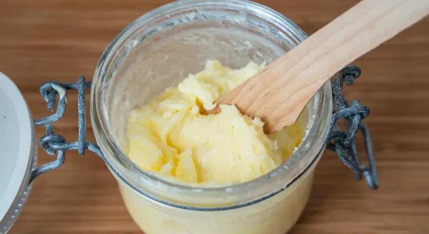 Frisch gemachte Butter in einem Glas, mit einem Holzspatel zum Butter selber machen.