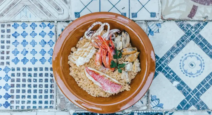 Un saporito cous cous di pesce con gamberi, calamari, cozze e triglia, guarnito con prezzemolo fresco.