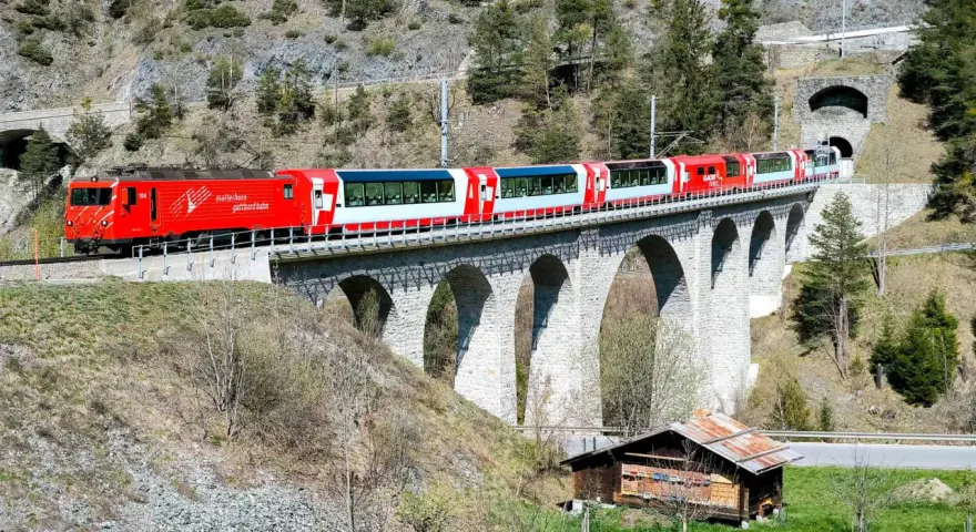 The red and white Glacier Express train travels across a stone viaduct, a scenic journey from Chur to Zermatt.