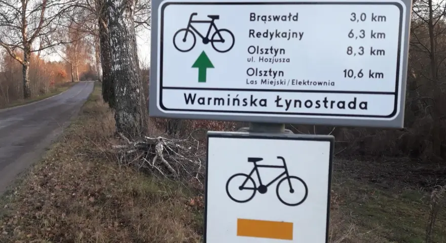 Znak drogowy informuje o odległościach do Brąswałd, Redykajn, Olsztyna i Lasu Miejskiego. To część szlaku Warmińska Łynostrada.