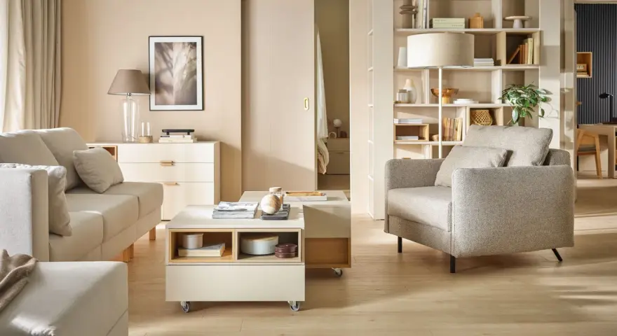 Nowoczesny salon po przemeblowaniu pokoju. Jasne meble, sofa, fotel, stolik kawowy i regał tworzą przytulną przestrzeń.