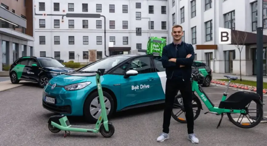 Ein Mann steht stolz neben einem Bolt Drive Auto, E-Scooter und Fahrrad. Er ist ein Bolt Fahrer, der umweltfreundliche Mobilität fördert.