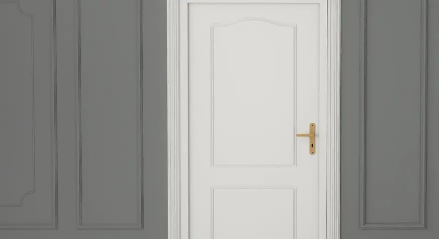 Białe drzwi z ozdobną listwą opaskową do drzwi i złotą klamką, na tle szarej ściany z panelami.
