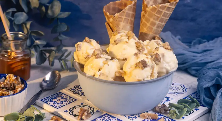 Schüssel mit Eiscreme, garniert mit Nüssen und Honig. Ein Glas Honig und Waffelhörnchen im Hintergrund. Ein süßer Genuss: Eis mit Honig statt Zucker.