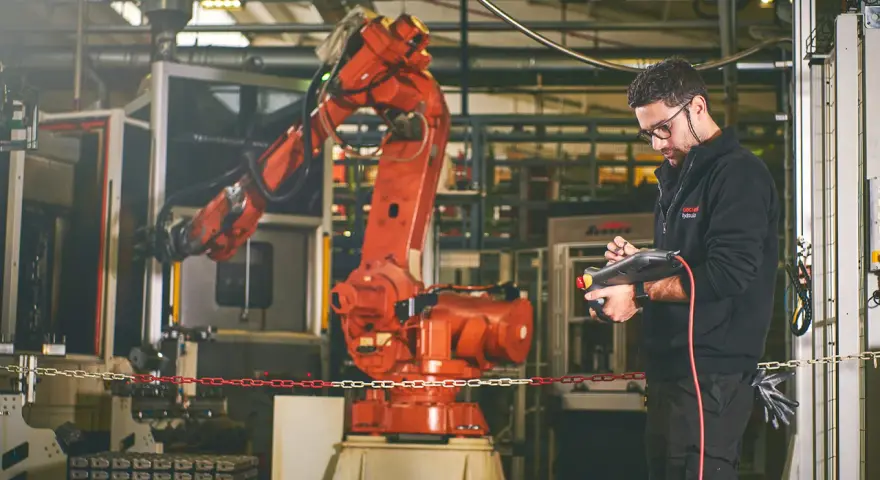 Un tecnico controlla un braccio robotico rosso in una fabbrica, dimostrando la meccatronica cos'è: l'integrazione di meccanica, elettronica e informatica.