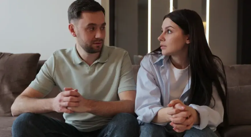 Un couple, peut-être un peu psycho, se regarde intensément, les mains jointes, sur un canapé.