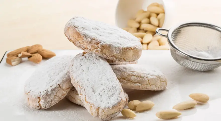 Dolce di Siena cosparso di zucchero a velo, con mandorle e setaccio sullo sfondo.