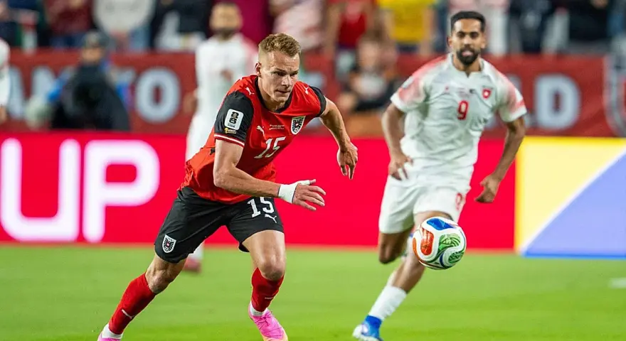Jugadores de fútbol en acción. El número 15 de Austria corre con el balón, mientras otro jugador se acerca. ¿Quién juega hoy?