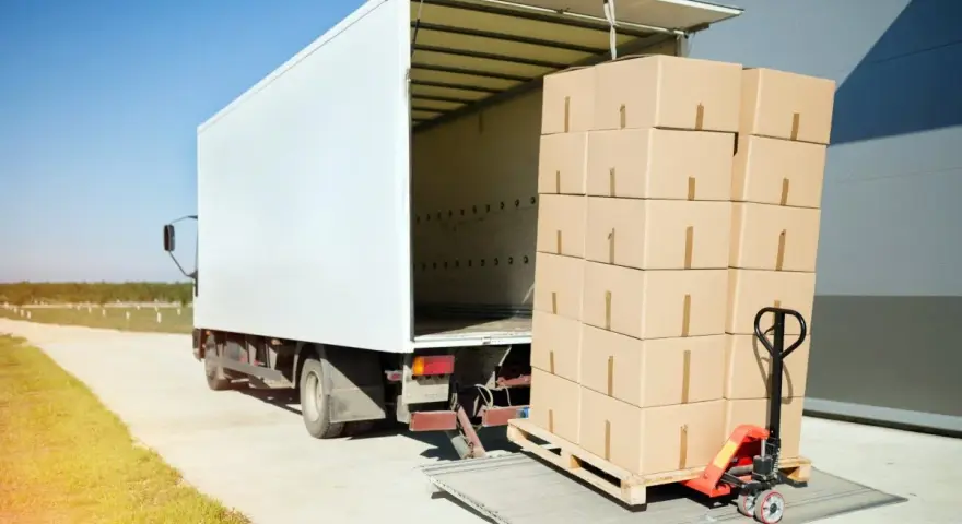 Stos kartonów na palecie, gotowy do załadunku do białej ciężarówki. Ubezpieczenia cargo chronią takie przesyłki.