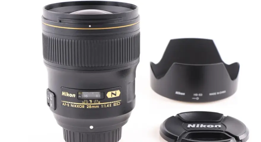 Obiektyw AF-S NIKKOR 28mm 1:1.4E ED z osłoną przeciwsłoneczną i deklem. Jasne oznaczenia obiektywów Nikon.
