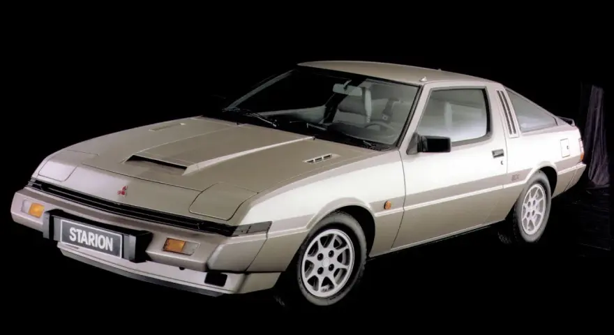 Klasyczny Mitsubishi Starion w kolorze szampańskim, z charakterystycznym wlotem powietrza na masce i sportowym nadwoziem coupe.