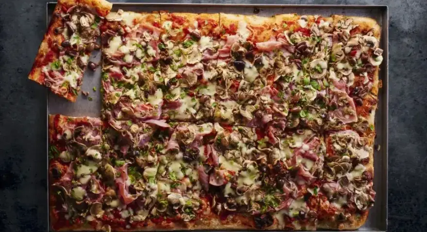 Oto najlepsza pizza przepis: prostokątna, obficie posypana pieczarkami, szynką i oliwkami, z ciągnącym się serem.