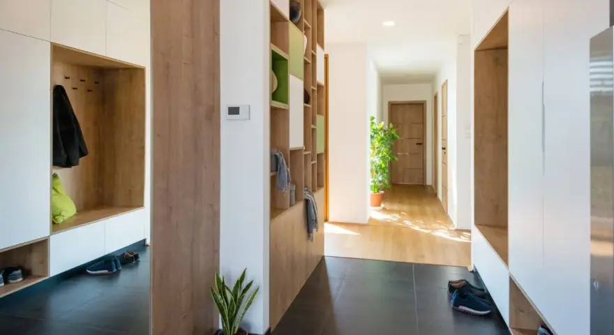 Ingresso moderno con armadi bianchi e legno, mensole a giorno per arredare ingresso, scarpe e piante.