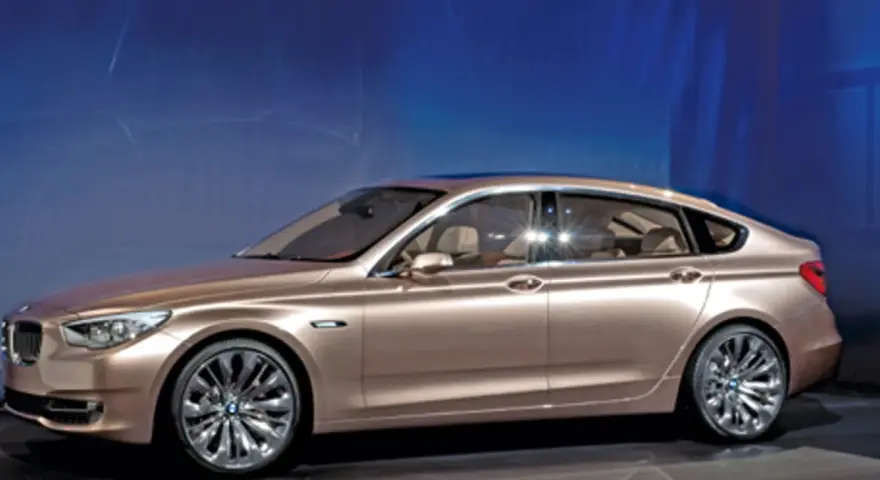 Eleganckie, złote bmw gt z przyciemnianymi szybami i chromowanymi felgami stoi na tle niebieskiej ściany.