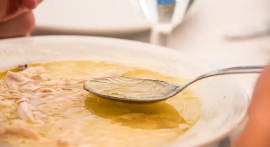 Caldo de pollo casero en un plato blanco con una cuchara.