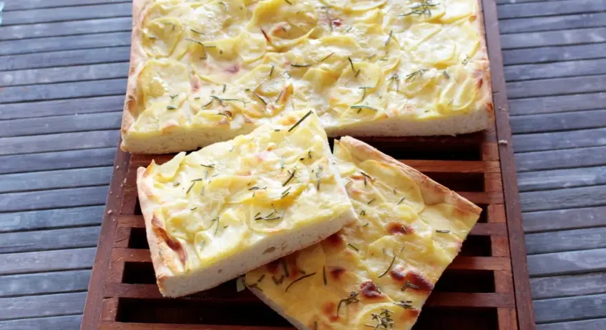 Focaccia con lievito istantaneo, ricca di patate e rosmarino, servita su un tagliere di legno.