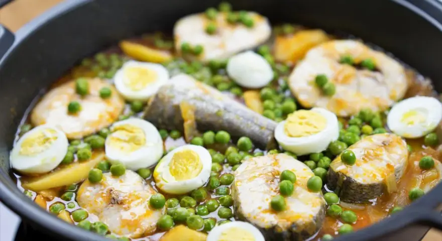 Merluza con guisantes y huevos duros en una sartén. Un plato casero y reconfortante.