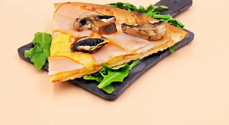 Kawałek pysznej pizzy capriciosa z szynką, serem i pieczarkami na ciemnej desce, ozdobiony rukolą.