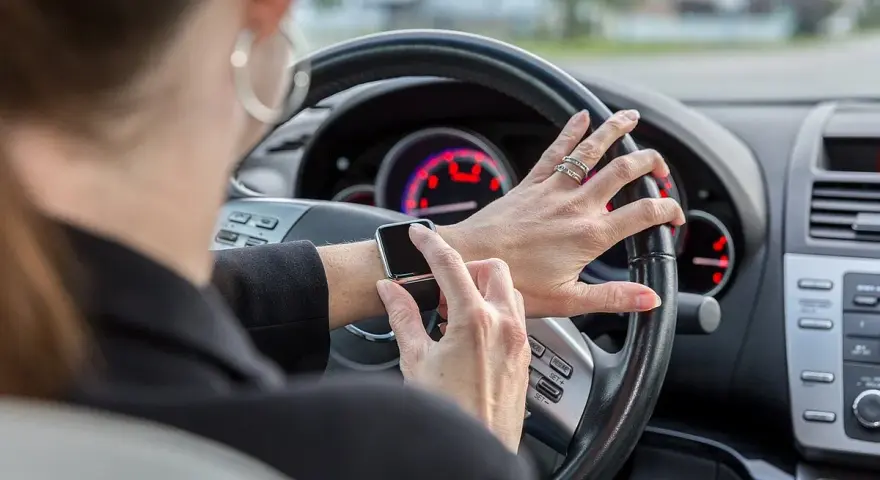Frau tippt auf ihre Smartwatch am Steuer. Handy am Steuer Strafe vermeiden!