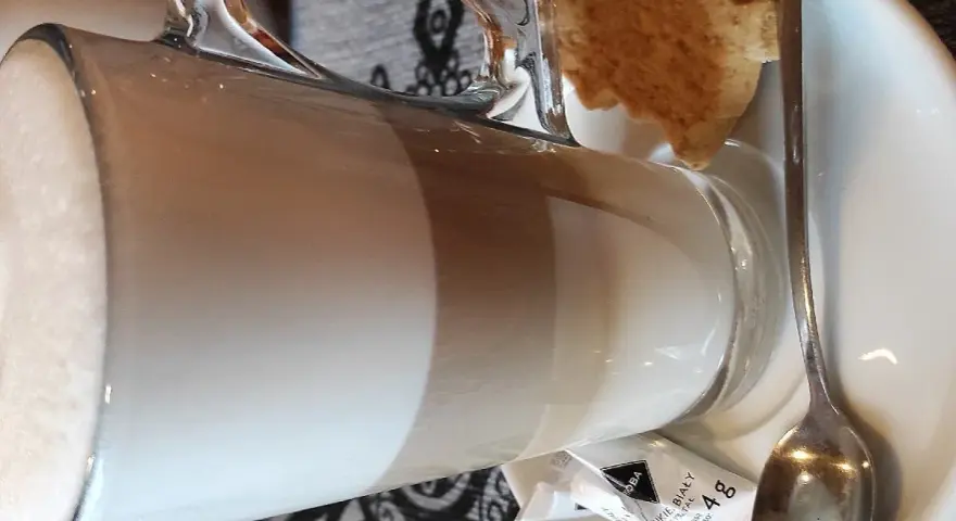 Kawa latte w szklance, obok ciasteczko i cukier. Idealna na przerwę w karczmie u wróbla menu.