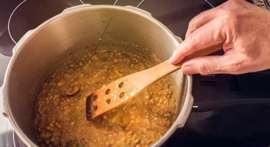 Lentejas deliciosas cocinándose en olla express, removidas con cuchara de madera.