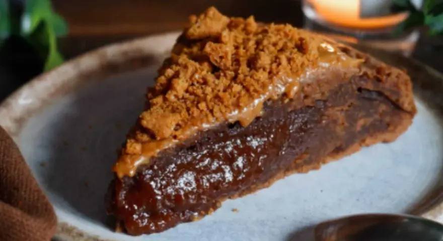 Une part de gâteau speculoos, riche et gourmande, garnie de miettes de biscuits et d'une sauce caramel.