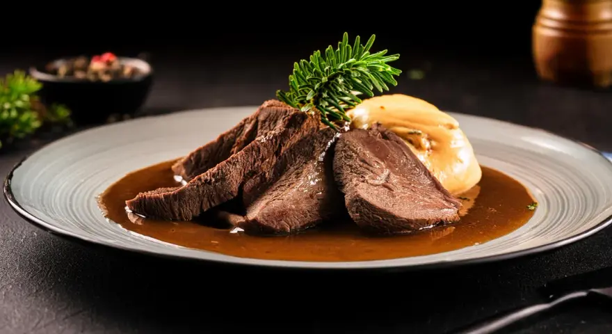Zartes Tafelspitz-Rezept auf einem Teller mit Sauce, Beilage und Rosmarinzweig.