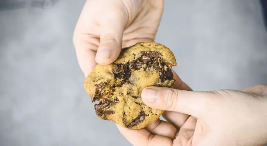Hände halten einen frisch gebackenen American Cookie mit geschmolzener Schokolade. Perfekt zum amerikanischen Cookies backen!