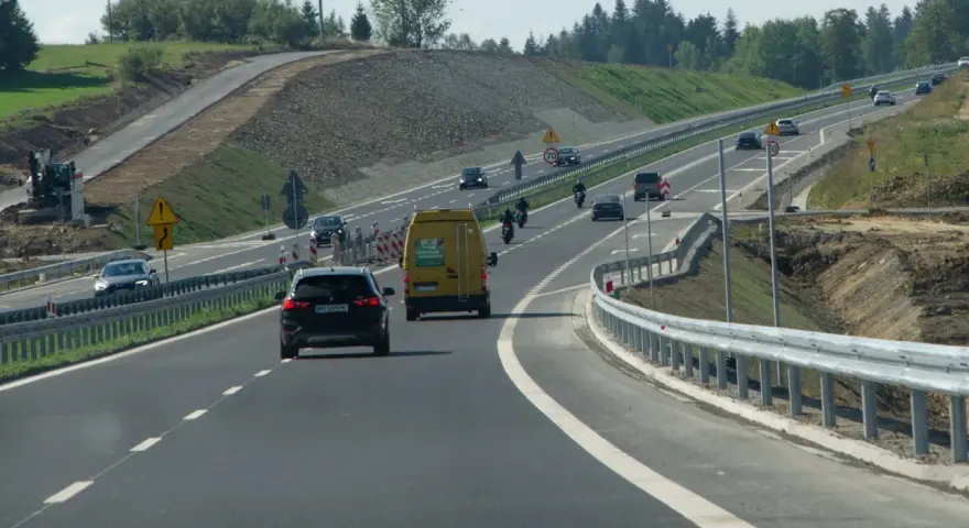 Droga ekspresowa z samochodami i motocyklami, gdzie panuje bezpieczna prędkość. W tle widać prace budowlane.