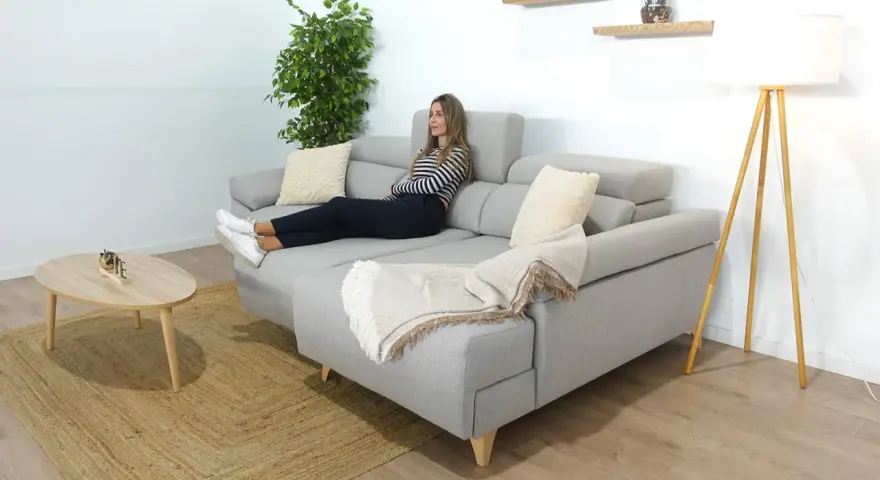 Mujer relajada en un sofá en medio del salón, con una manta y cojines.