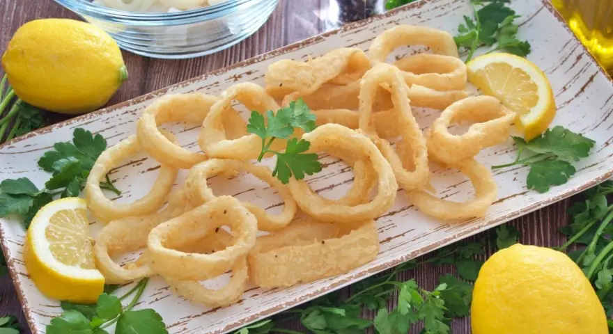 Calamares a la andaluza crujientes y dorados, servidos con limones frescos y perejil.