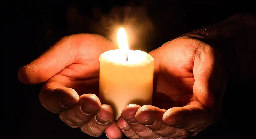 Hände halten eine brennende Kerze, ein Symbol für den Totensonntag, das Licht und Erinnerung spendet.