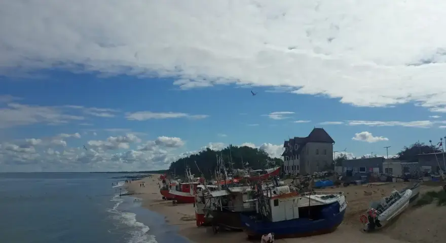 Chłopy trasa: łodzie rybackie na plaży, budynek z czerwonym dachem, morze i niebo z chmurami.
