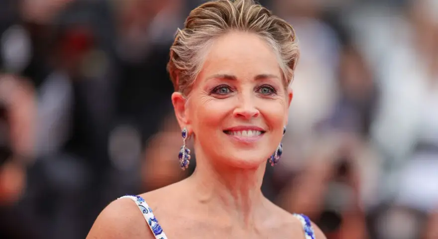 Sharon Stone luce un elegante corte bixie, con pendientes de zafiro y un vestido blanco con detalles azules.