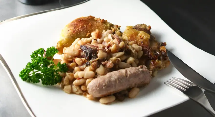 Un plato de el cassoulet con pollo crujiente, salchicha y perejil fresco.