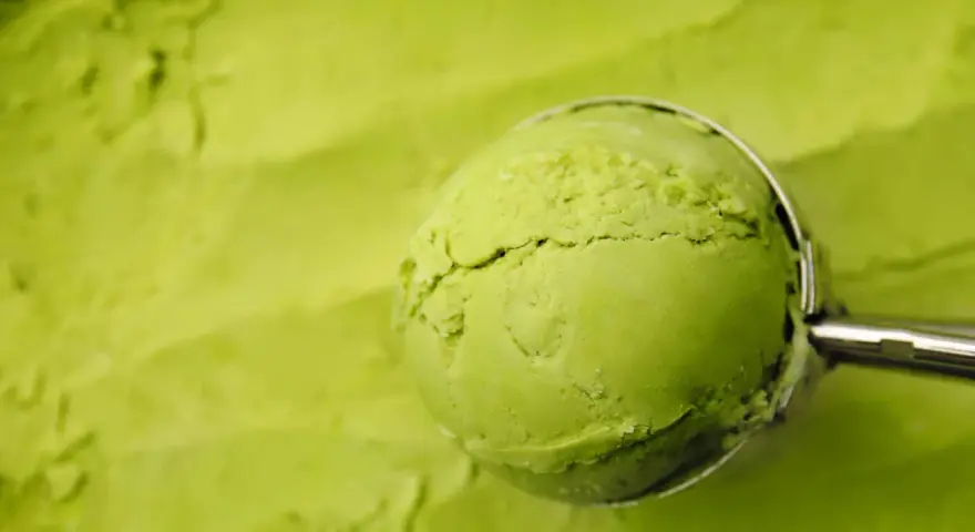 Eine Kugel cremiges Matcha-Eis wird mit einem Löffel aus einer Schüssel gehoben. Perfekt für ein erfrischendes Matcha Eis Rezept.