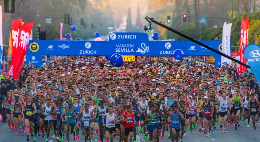 Multitudinaria salida del maratón Sevilla 2026, con miles de corredores bajo el arco de meta.